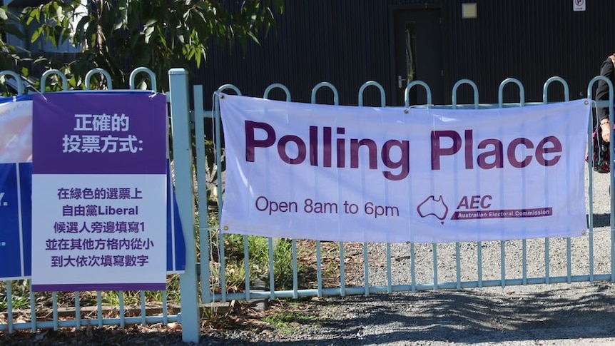 A poster in purple and white is attached to a fence next to an official AEC polling poster.