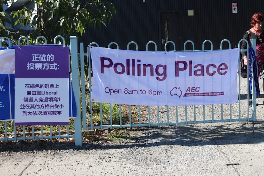 A poster in purple and white is attached to a fence next to an official AEC polling poster.