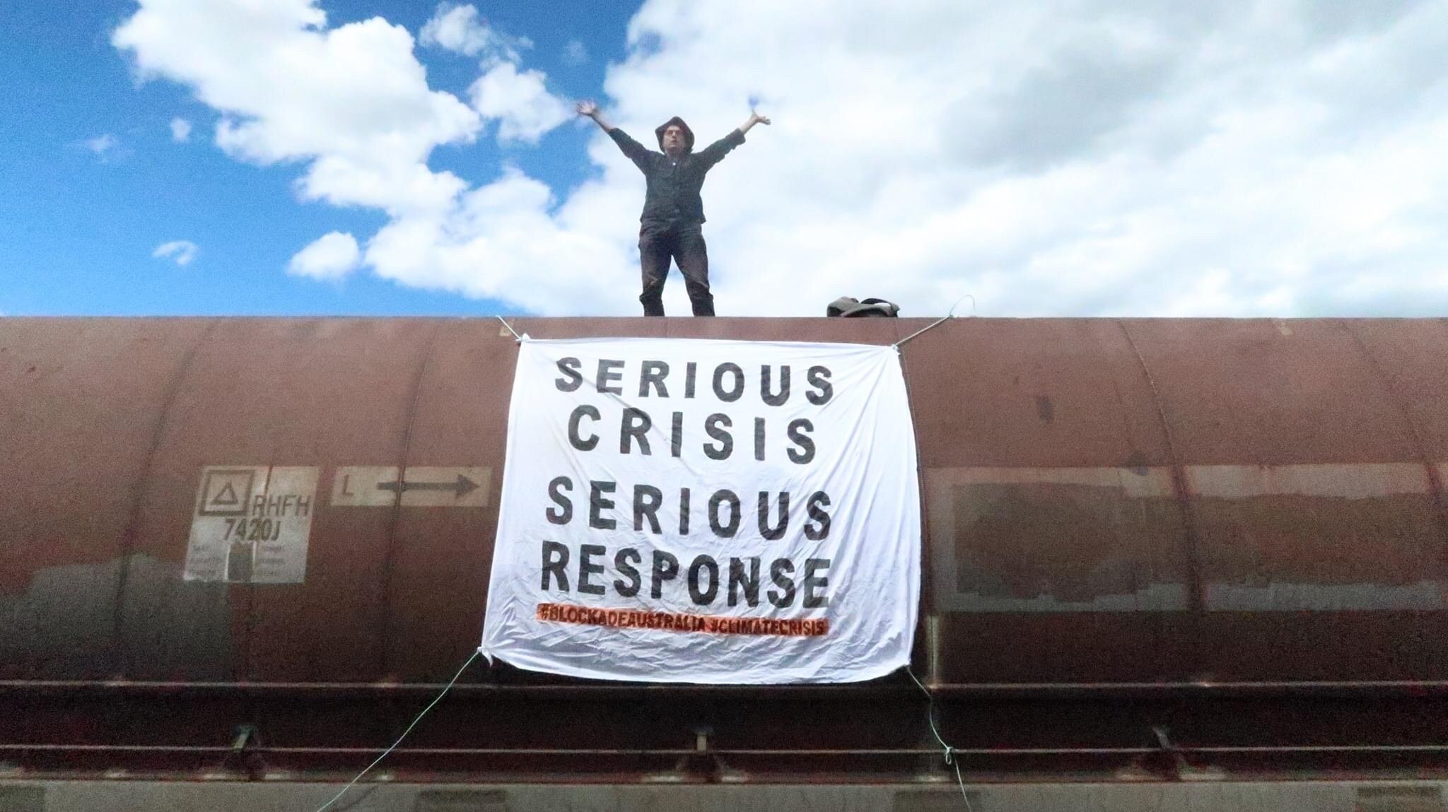 a man stands on a coal wagon with arms outstretched and a sign on wagon saying serious crisis, serious response
