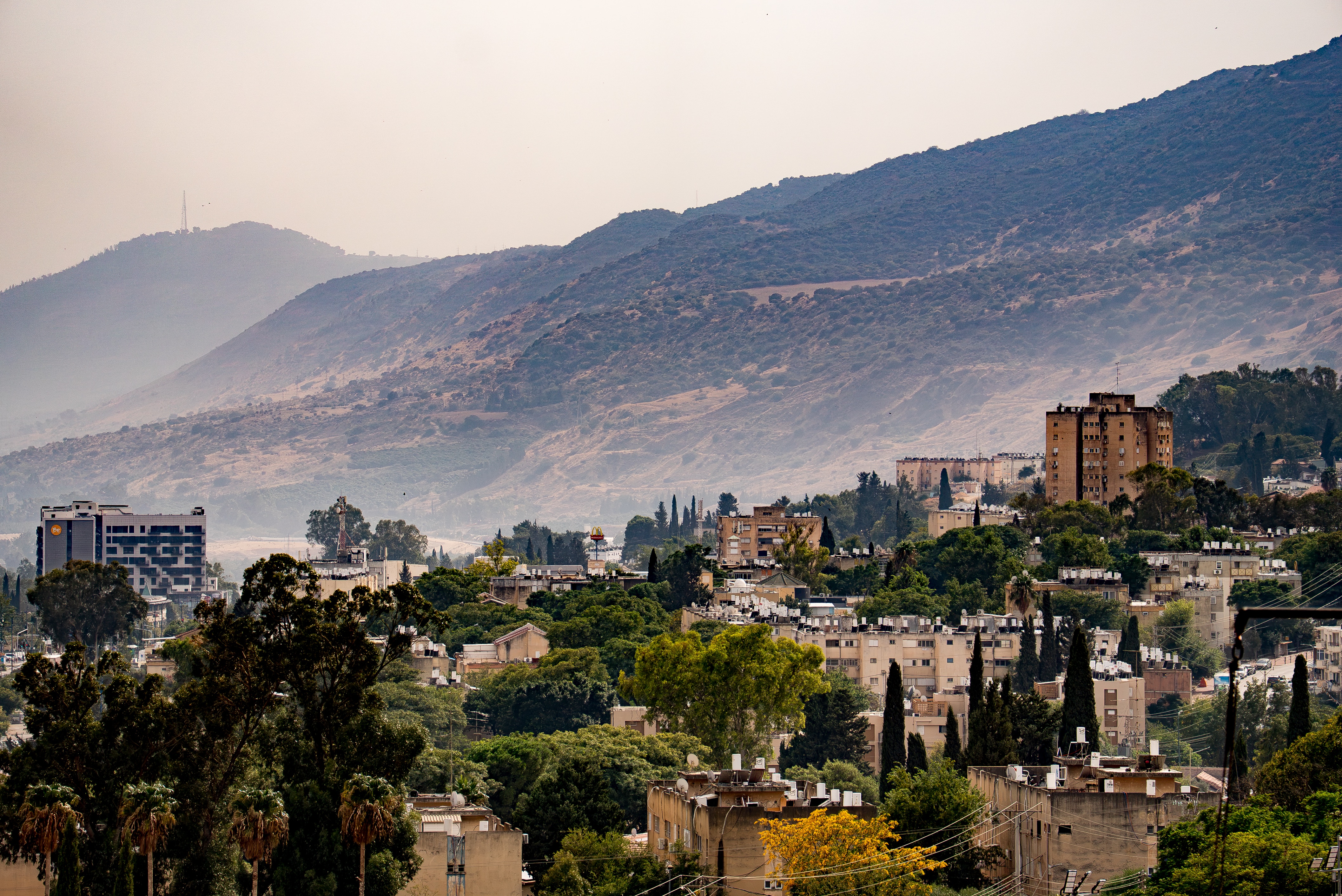 Buildings among trees below a large ridge that rises above the city in the background.