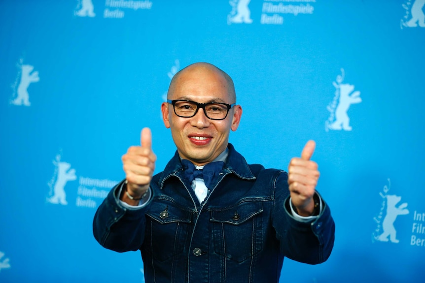 A man gives two thumbs up on the red carpet at a film premiere