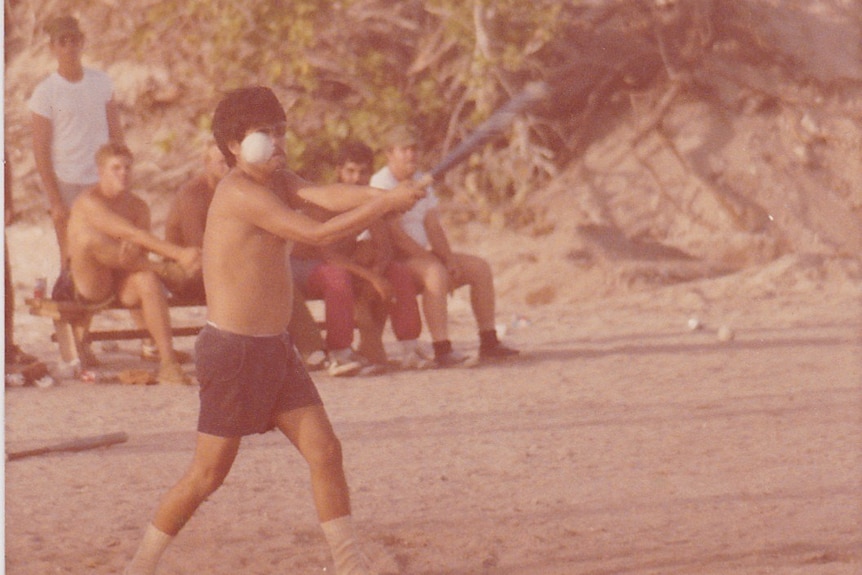 A shirtless man swings and hits a baseball on Enewetak.