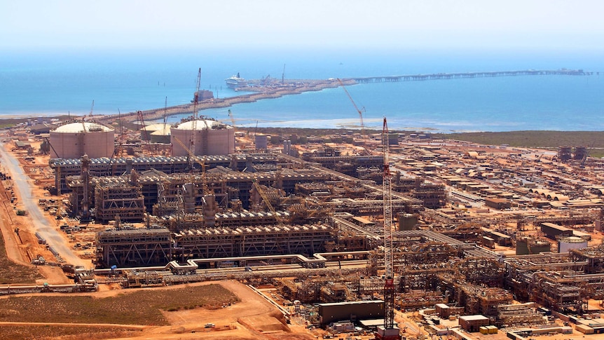 A gas refinery on the red dust of the WA coast with aqua ocean in the background.