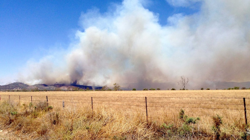 A rural landscape with a large amount of smoke rising from mountains in the distance