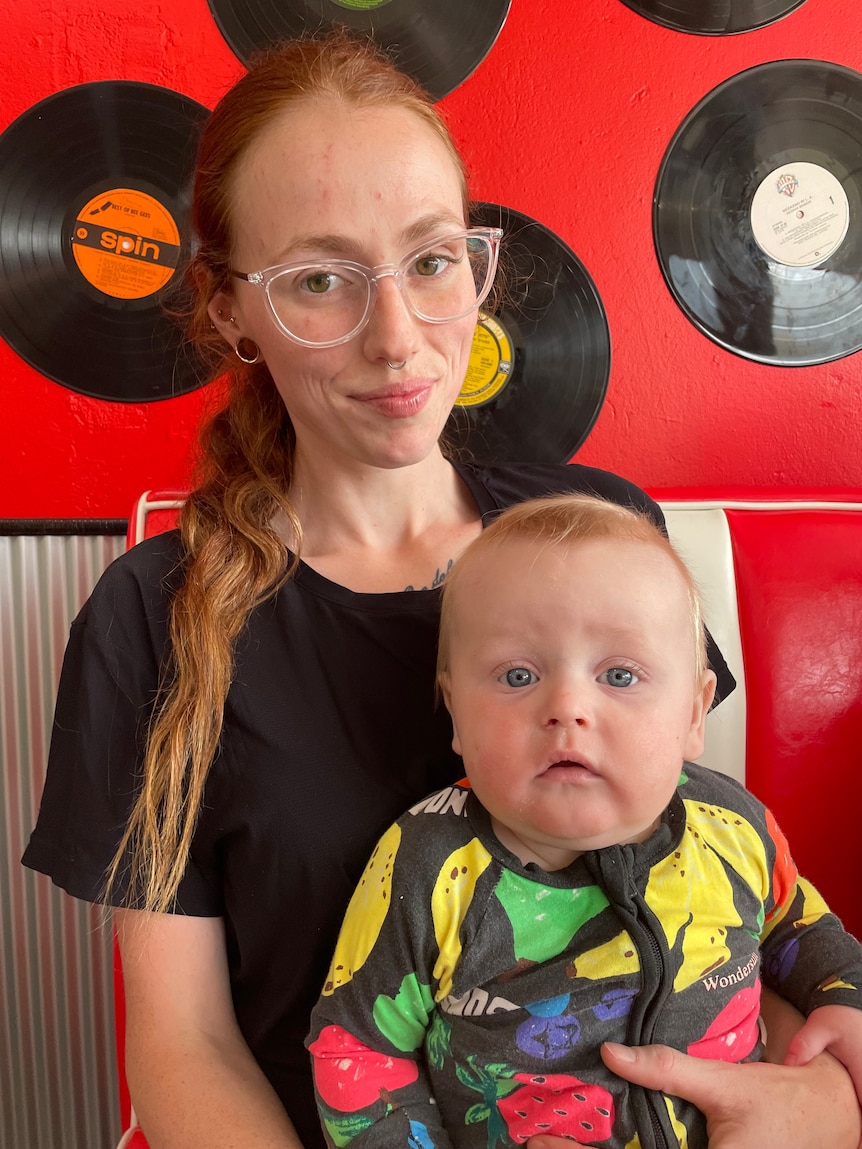 A woman with long red hair sits in a diner with a baby in her lap.