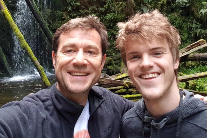 Two men in a selfie near a waterfall.