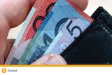 A wallet with a pink five dollar, blue ten dollar and red twenty dollar note sticking out