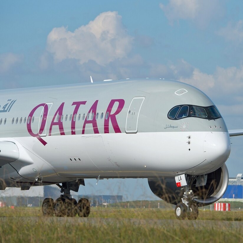 A Qatar Airways Airbus A350-900 on the tarmac on a lightly cloudy day.