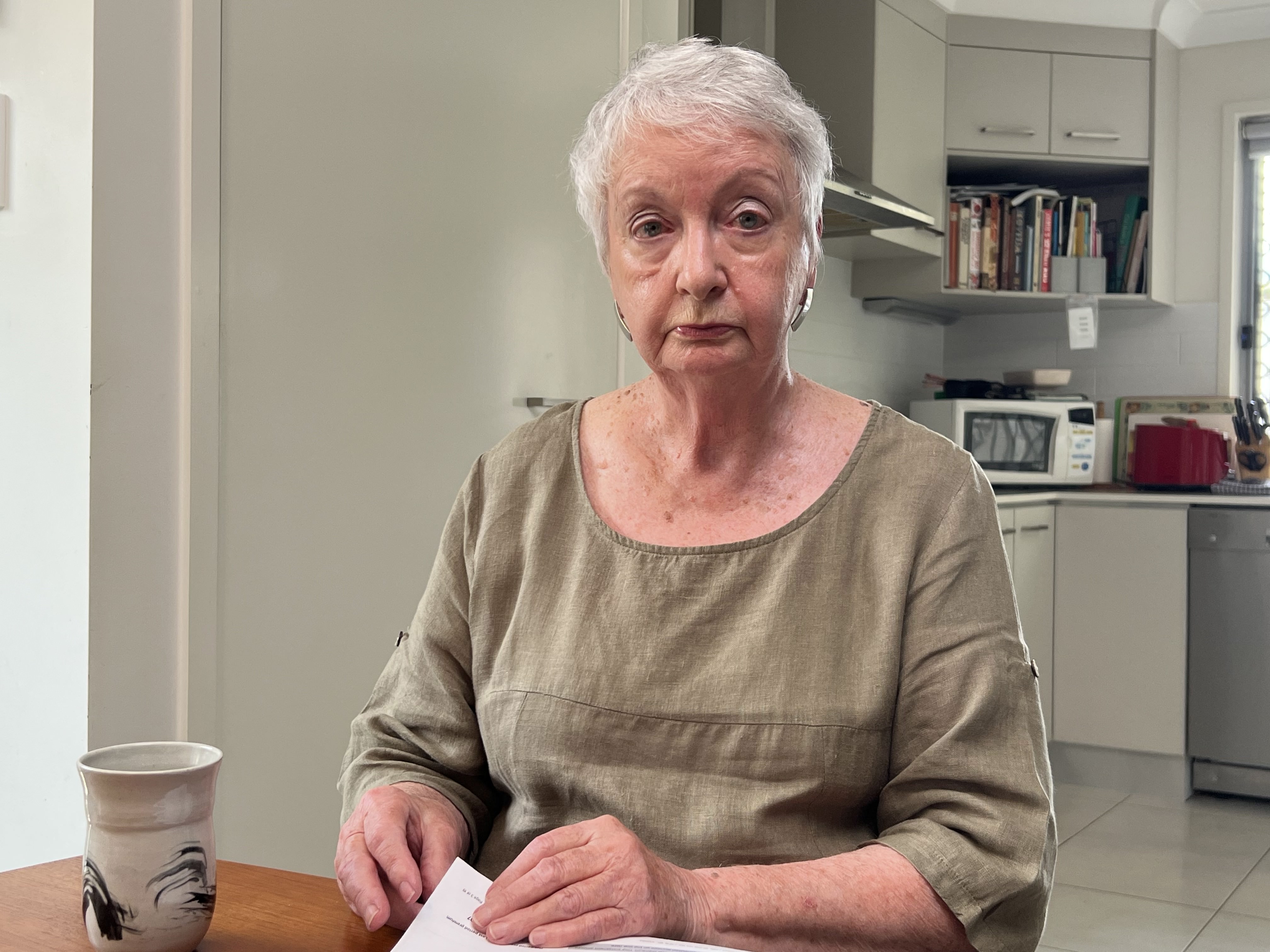 a woman sits at a kitchen table with a serious expression