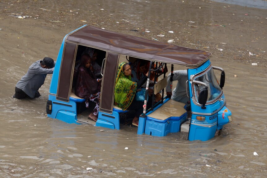 A rickshaw driver and a volunteer push a rickshaw stuck in a flooded road after a heavy rainfall.