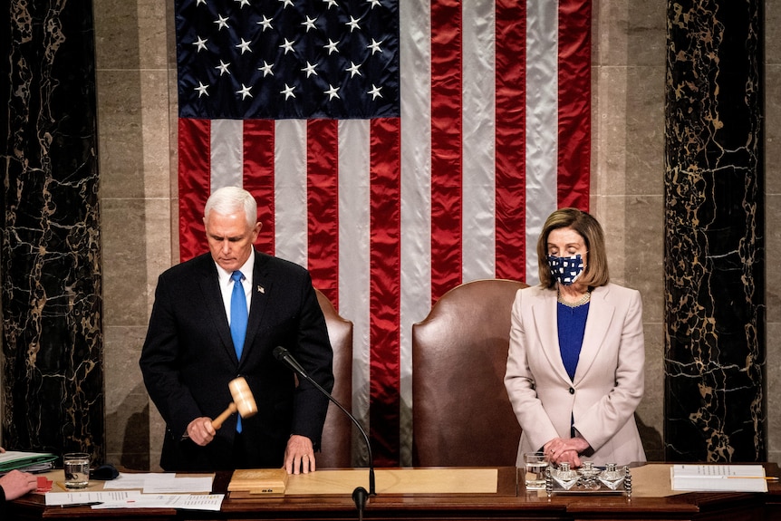 Mike Pence and Nancy Pelosi stand in front of a US flag in the US Capitol.