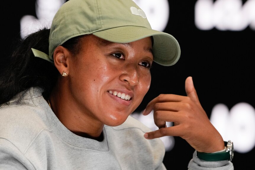 Naomi Osaka holds her hand to her head like a phone or a shaka during a press conference at the Australian Open.