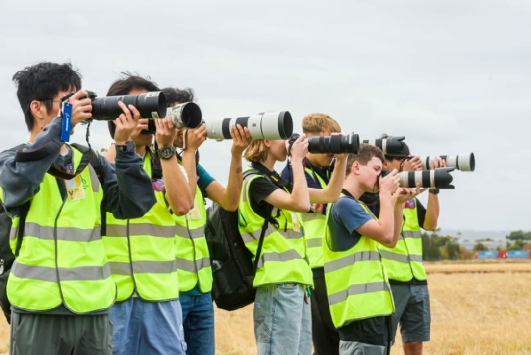Una fila de hombres con chalecos de seguridad amarillos y sosteniendo cámaras con grandes teleobjetivos.