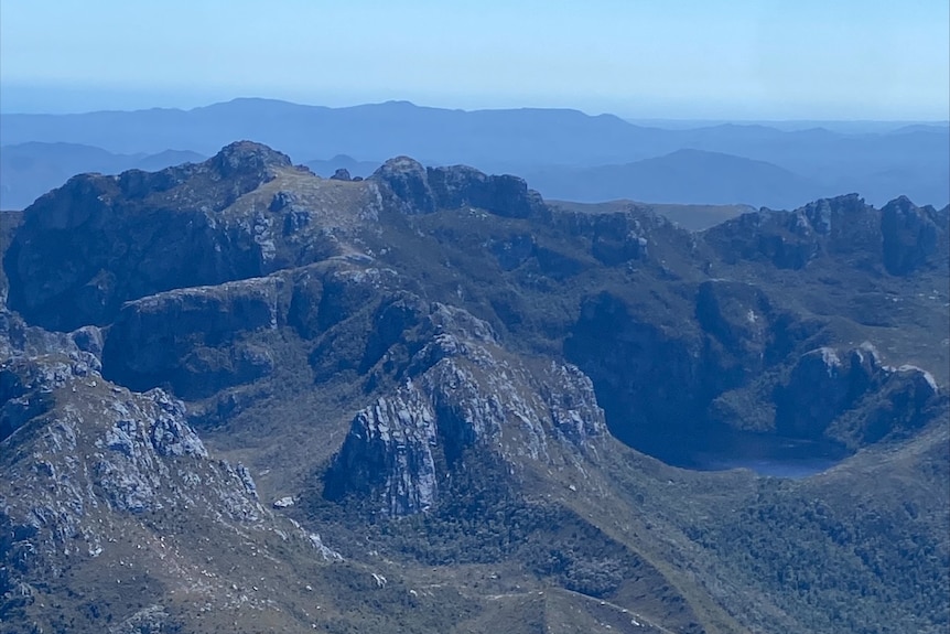 A dramatic mountain range is covered in greenery as it reaches for the blue sky.