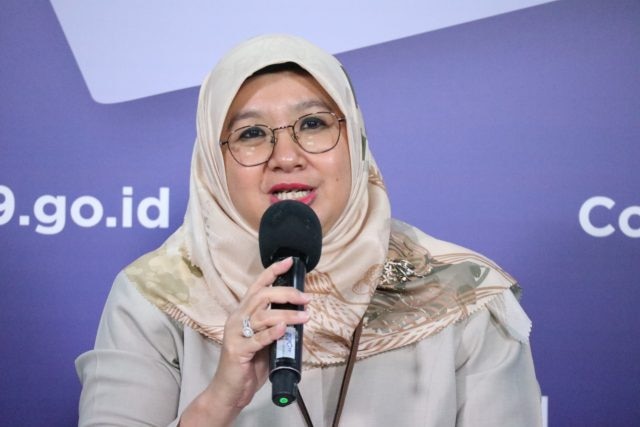A woman wearing a headscarf and glasses speaks into a microphone