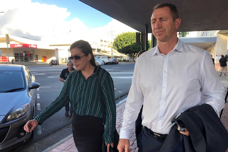 A woman wearing sunglasses walks with a man on a footpath.