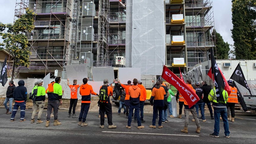 Protests stand on the street facing a building that is under construction