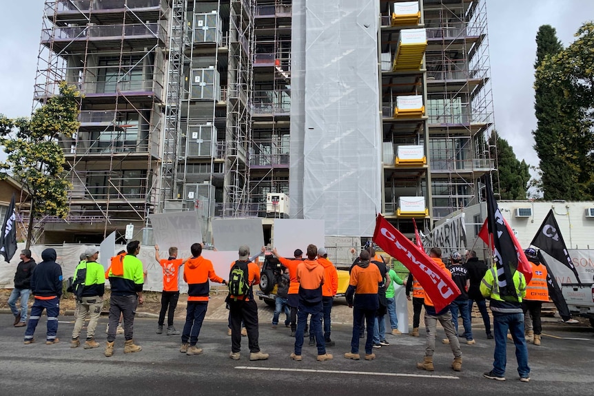 Protests stand on the street facing a building that is under construction