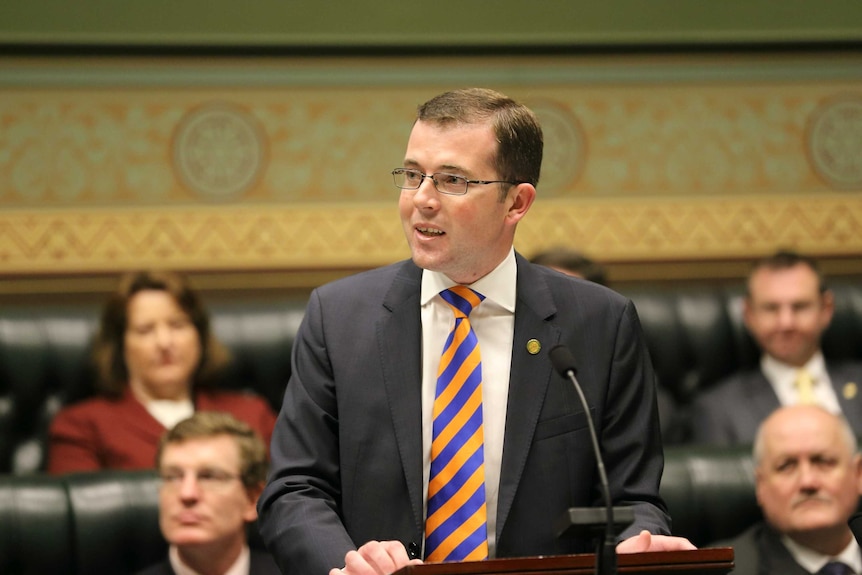 A man in a grey suit and a yellow and purple tie making a speech.