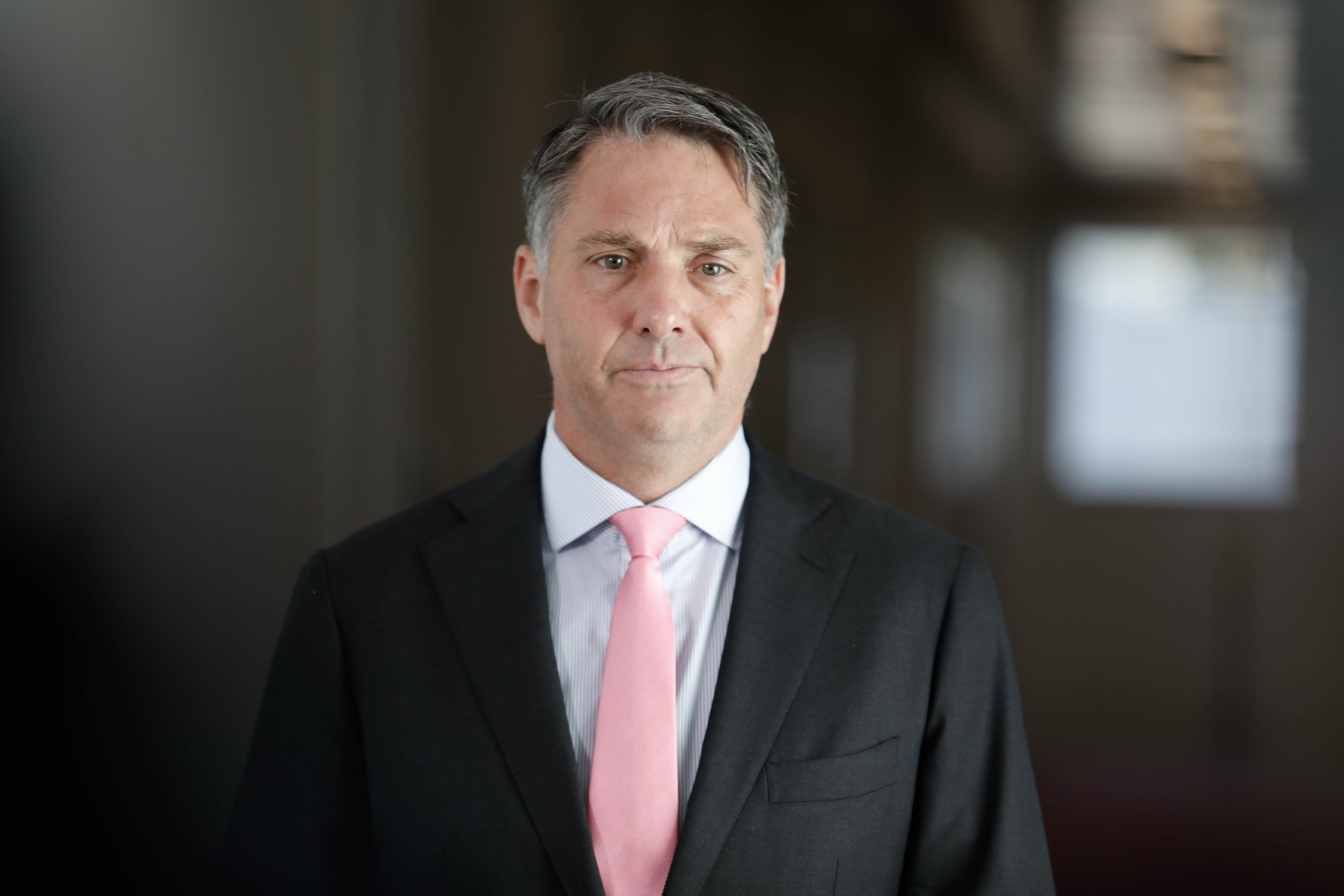 A sad man in a suit walks down a hall