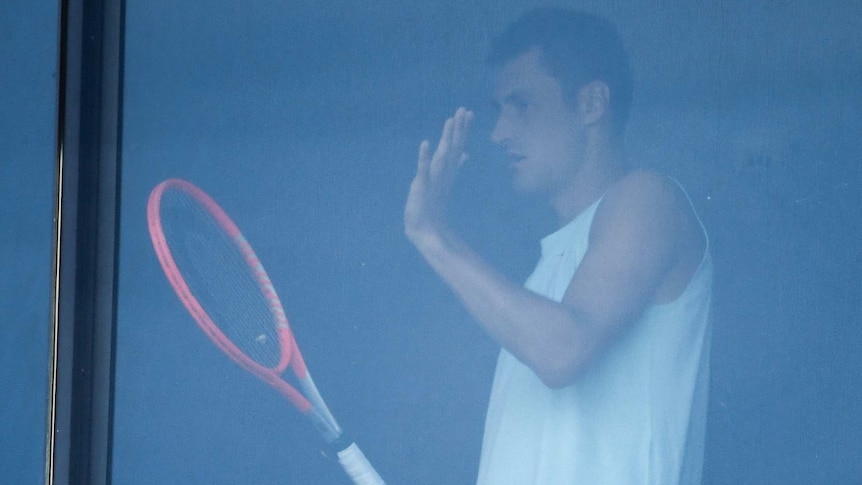 Bernard Tomic is seen through a hotel window playing with a tennis racquet