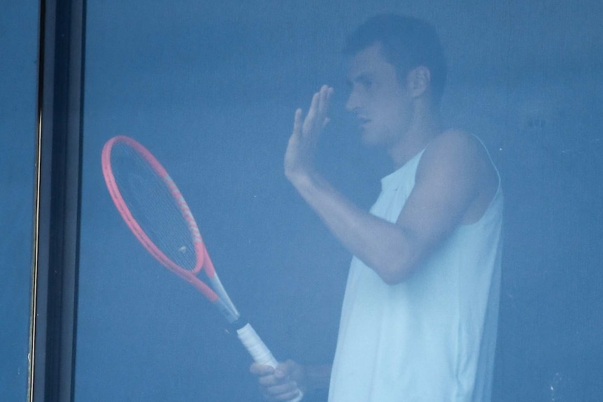 Bernard Tomic is seen through a hotel window playing with a tennis racquet