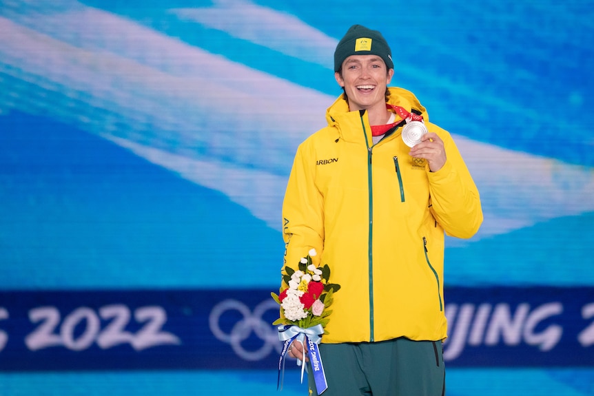 Scotty James smiles as he holds his silver medal in one hand and a bunch of flowers in the other.
