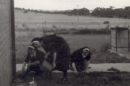 Three nuns crouch with buckets in a yard, working or playing at gardening.