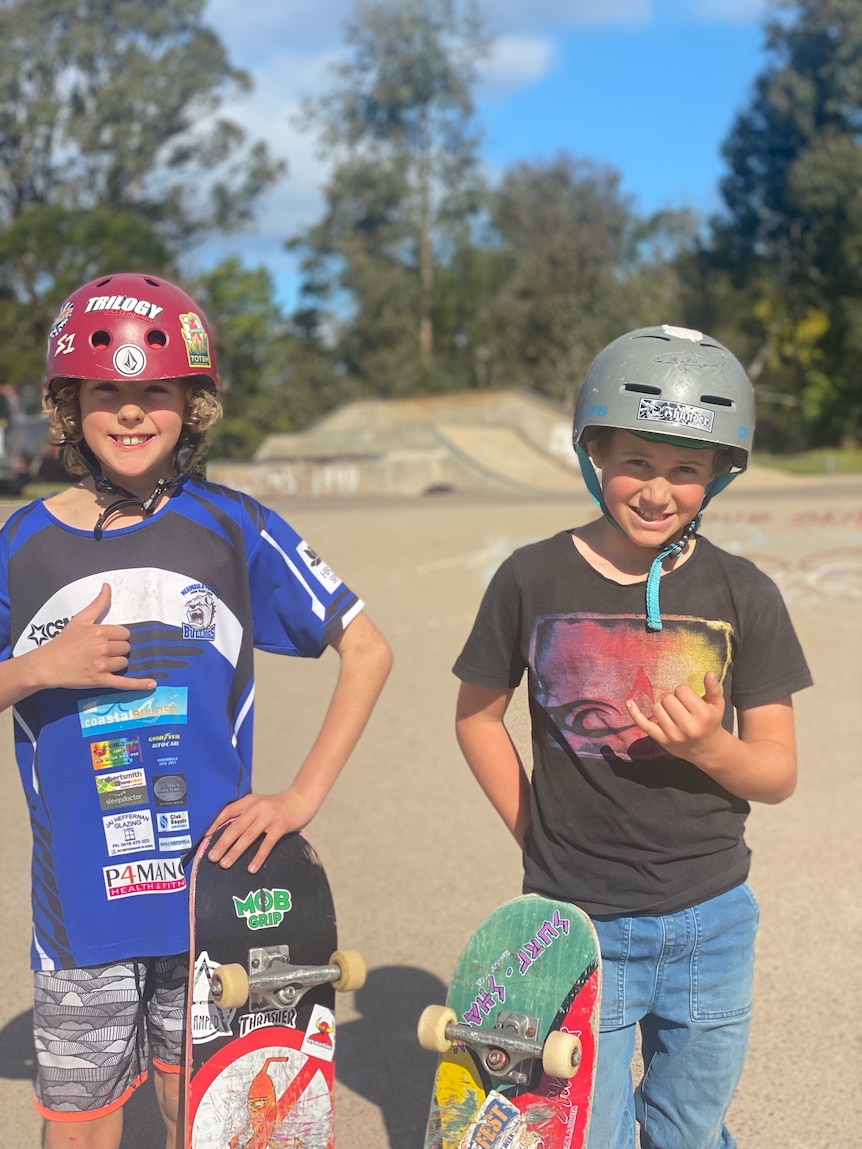 Two young boys with helmets and skateboards at a skate park.
