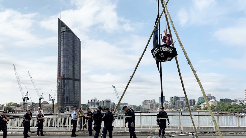 Woman from Extinction Rebellion suspends herself over Brisbane River from a tripod on Victoria Bridge.