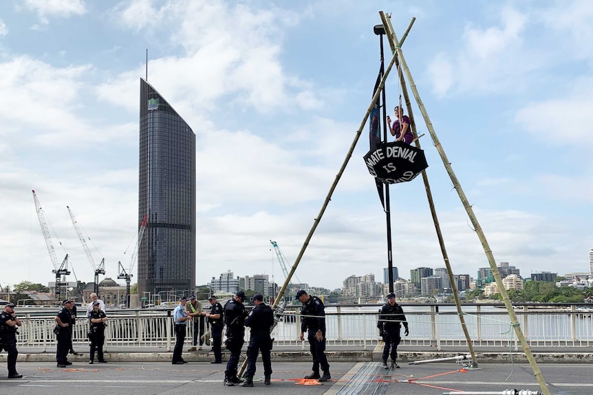 Woman from Extinction Rebellion suspends herself from a tripod on Victoria Bridge, with Brisbane River below