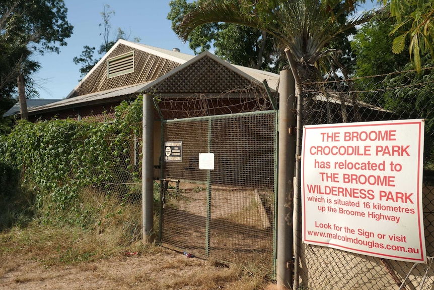 A fence runs in front of a build, covered in weeds and with a sign saying Broome Crocodile Park