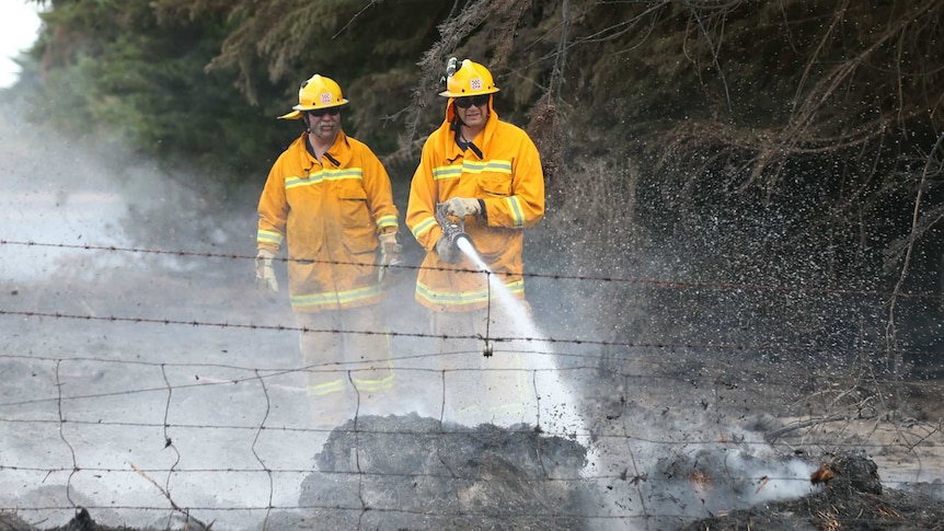 Two CFA firefighters use a hose to put out embers on a farm..