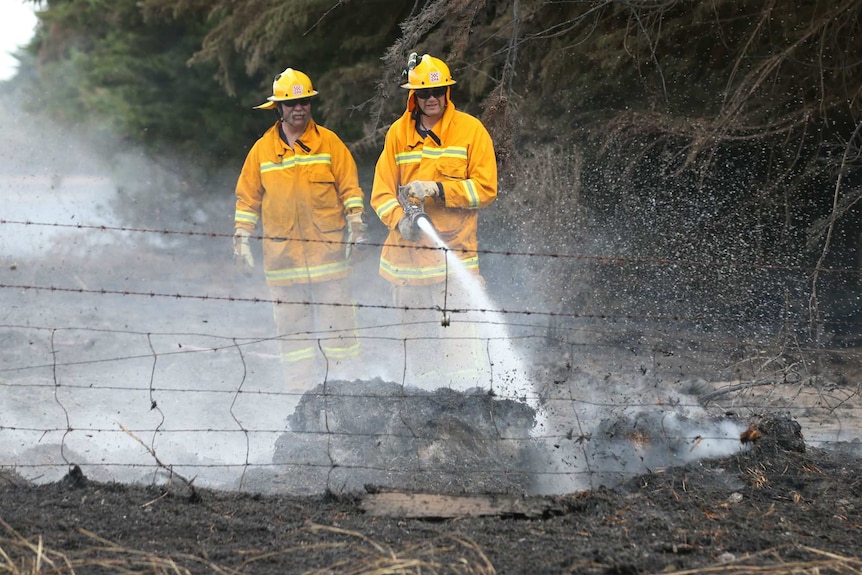 Two CFA firefighters use a hose to put out embers on a farm..