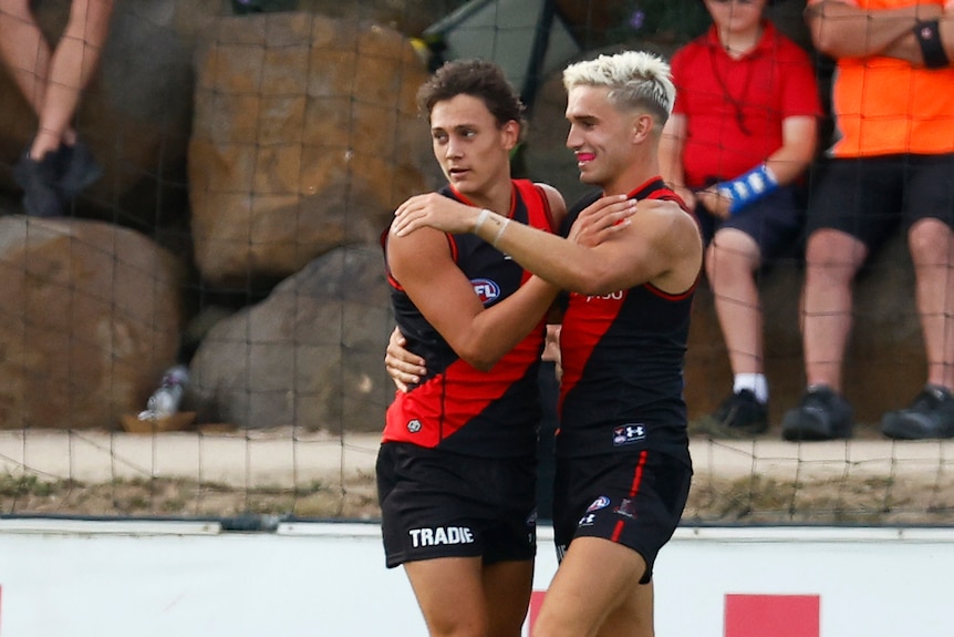 Two footballers in red and black hug on the football field.
