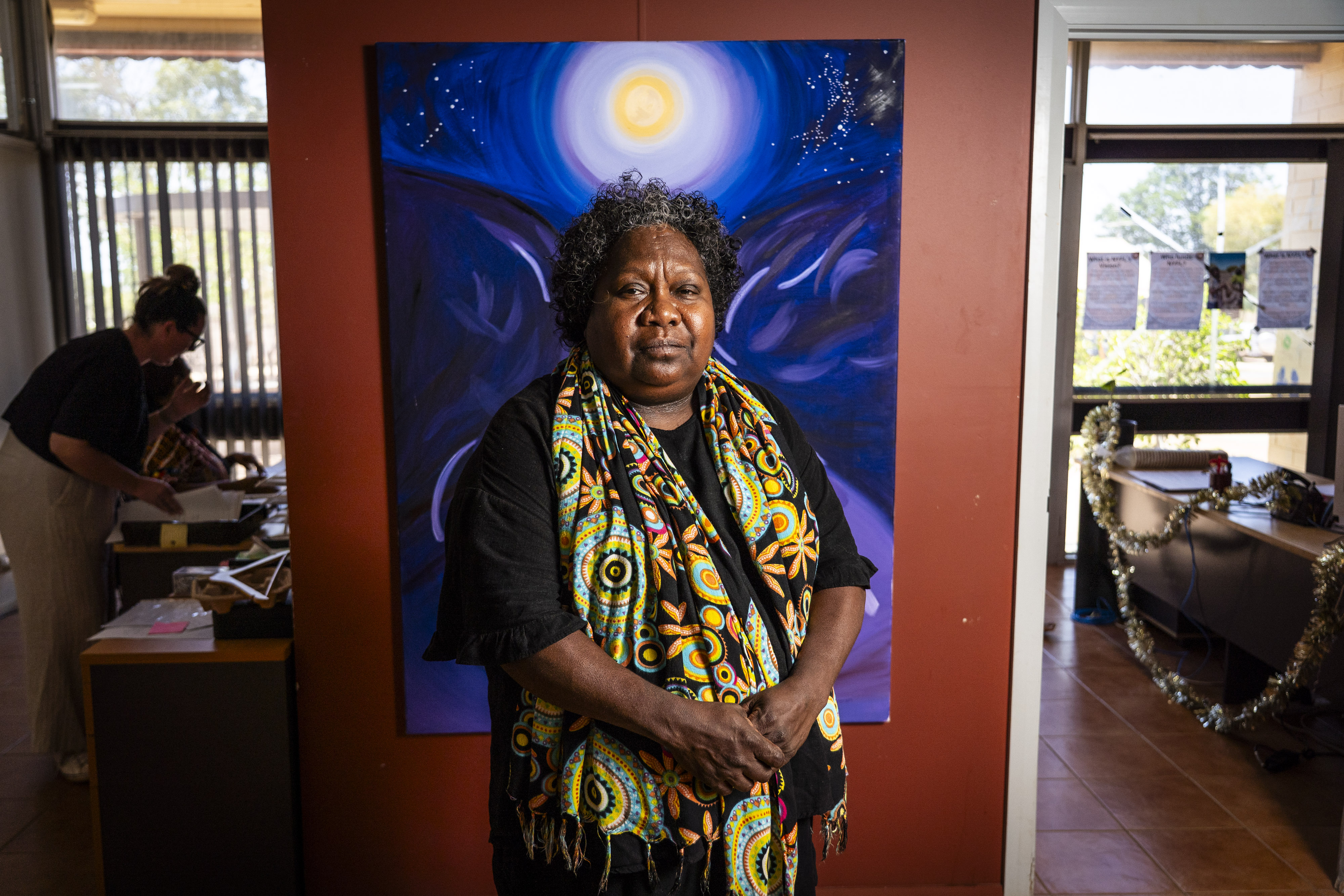 Uma mulher com um lenço fica em frente a uma obra de arte brilhante. 