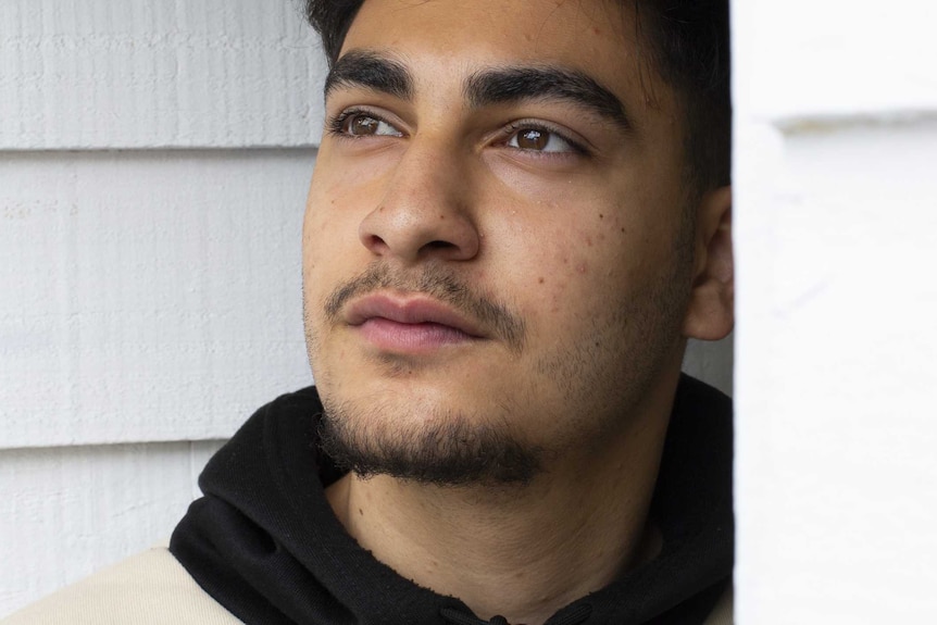 A young man looks into the distance in front of a white exterior wall