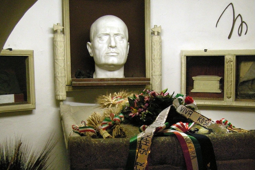 A tomb with a large white bust of a head and a piece of stone with flowers on it