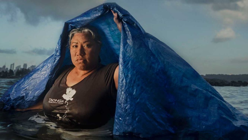 Latai Taumoepeau standing in chest-deep open water and holding a blue tarpaulin over her head