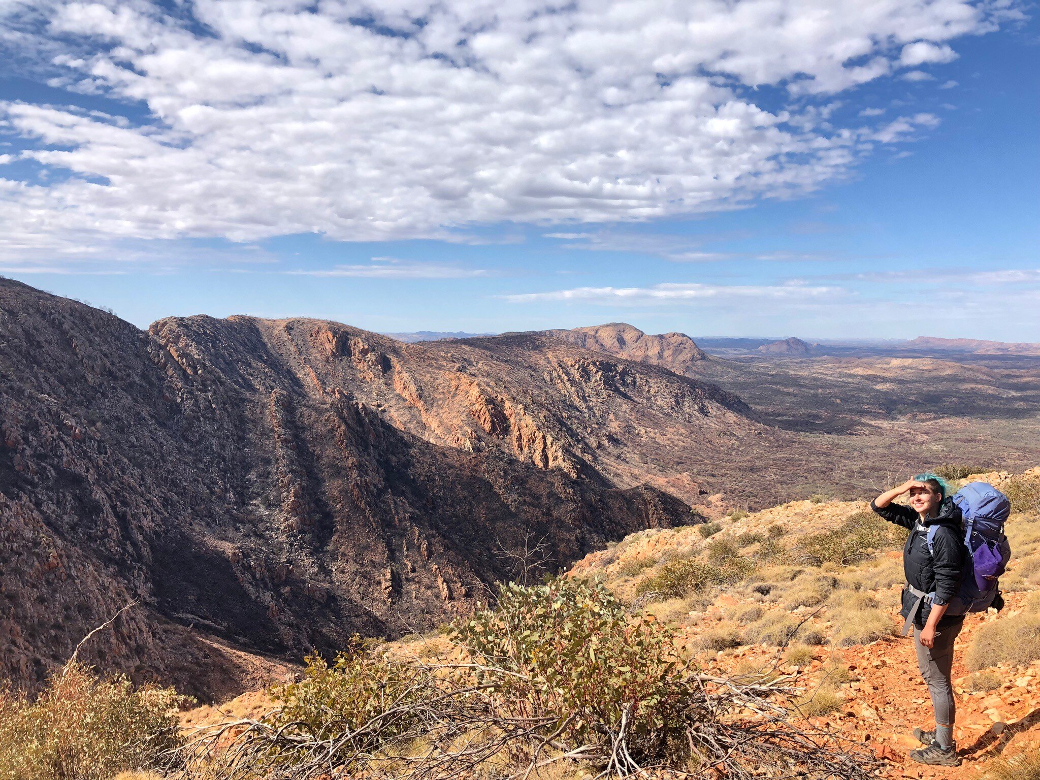A landscape shot of a valley with brown grass and mountains and blue sky. A person stands on the right of the picture