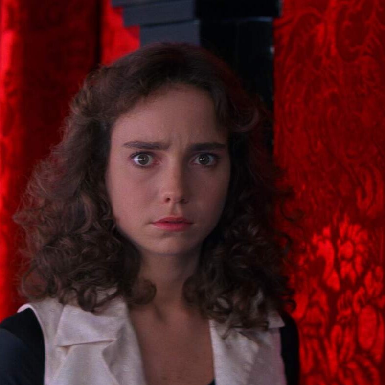 A still from the film Suspiria, with actress Jessica Harper with a concerned expression in front of a vivid red wall.