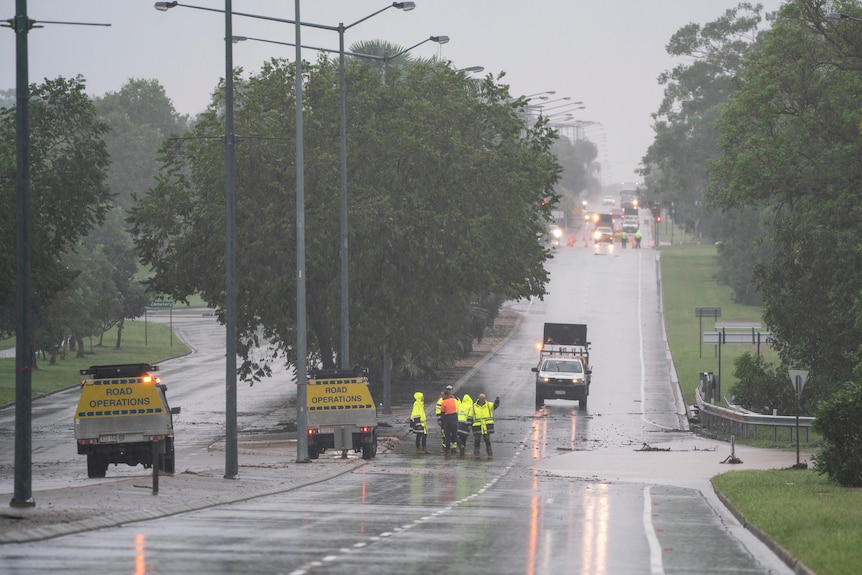 Traffic workers in bright colours are in the middle of a flooded road with signage telling motorists to be careful.