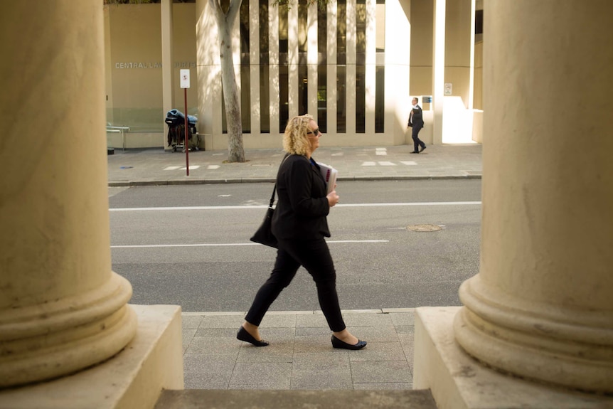 A wide shot of woman walking past two pillars on the street
