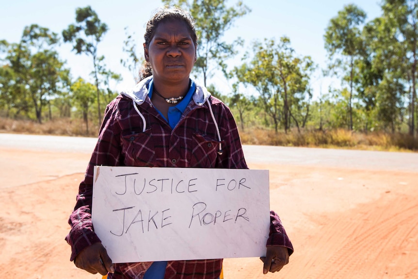 A woman holds a sign saying justice for jake roper.