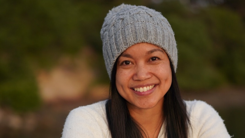 A young woman wearing a white sweater and a grey beanie smiles at the camera.