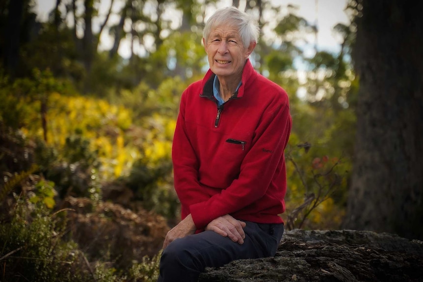 Andrew Lohrey sits on a log and smiles at the camera.