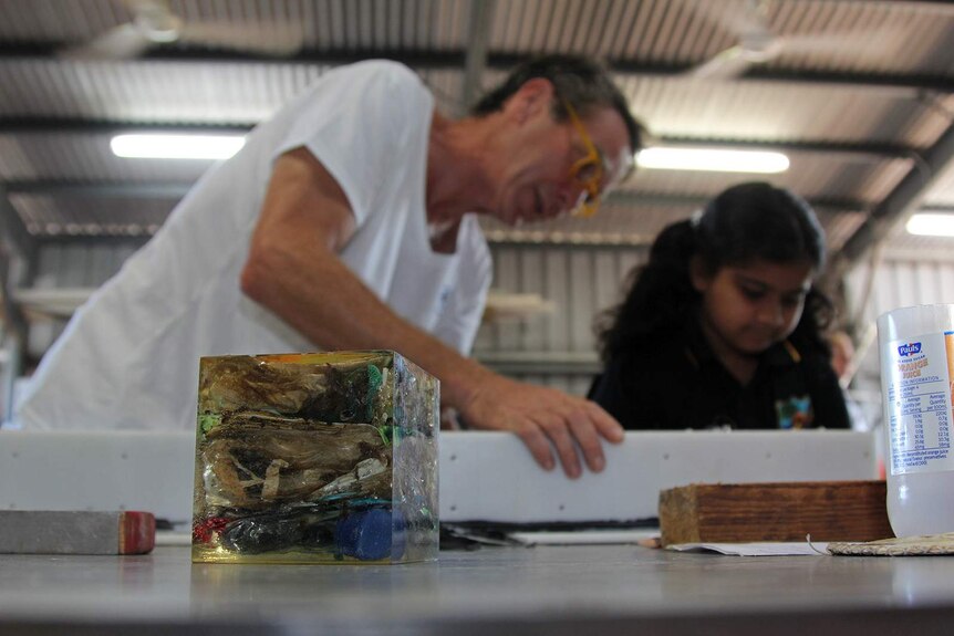 A photo of Harald Reichenbach standing next to a student, with a cube of compressed ocean waste in the foreground.
