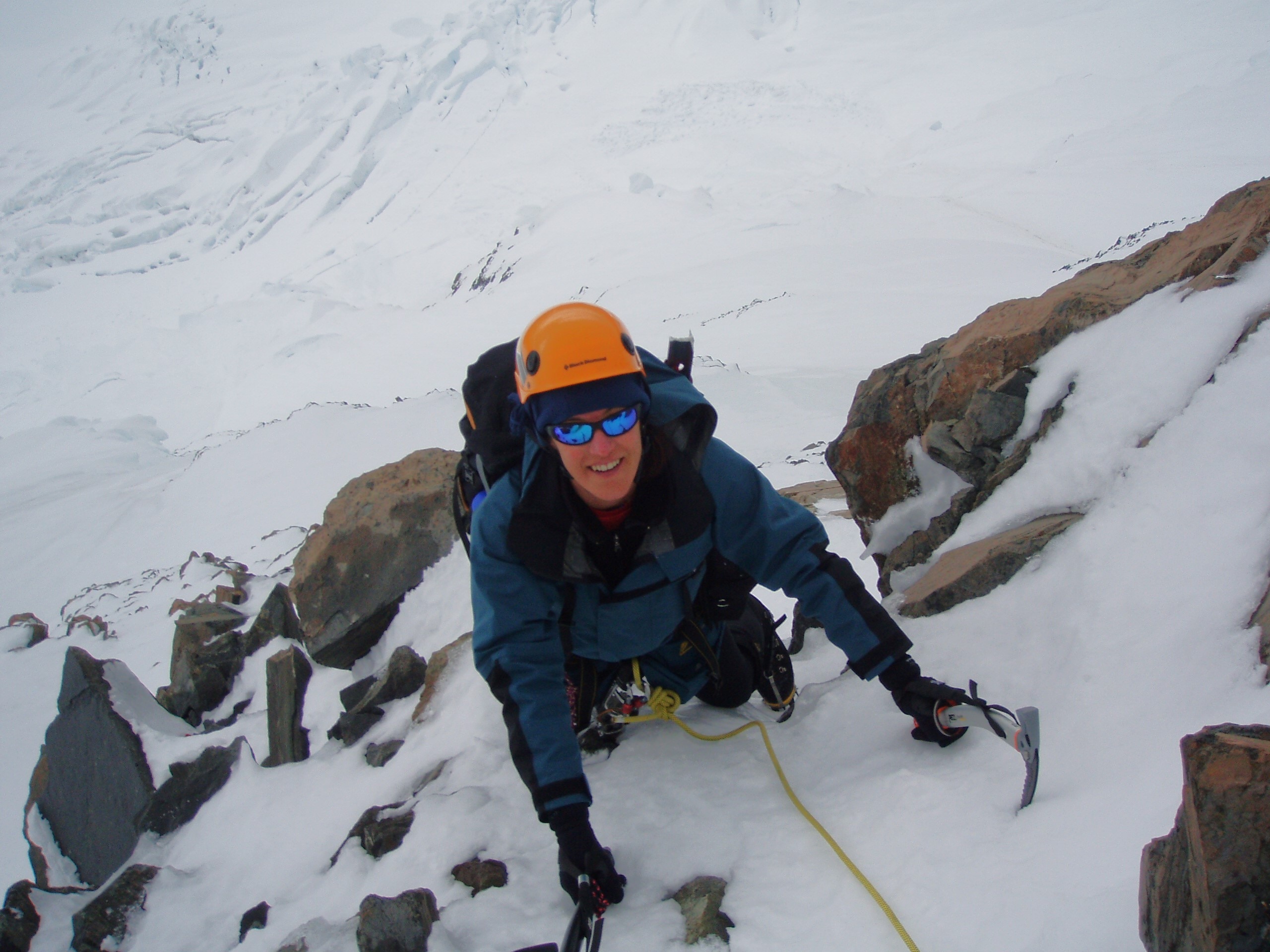 A woman uses as ice pick to climb a steep icy ledge