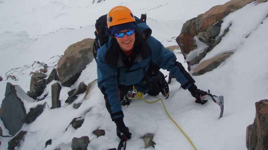 A woman uses as ice pick to climb a steep icy ledge