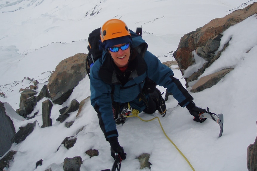 A woman uses as ice pick to climb a steep icy ledge